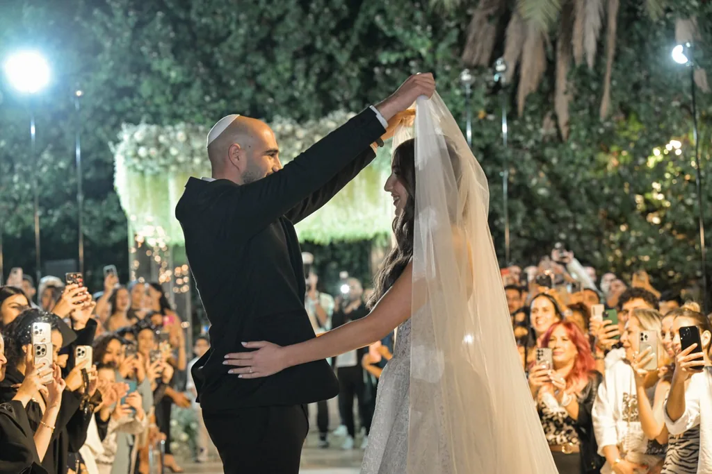 החתן מכסה את הכלה בהינומה מול האורחים
